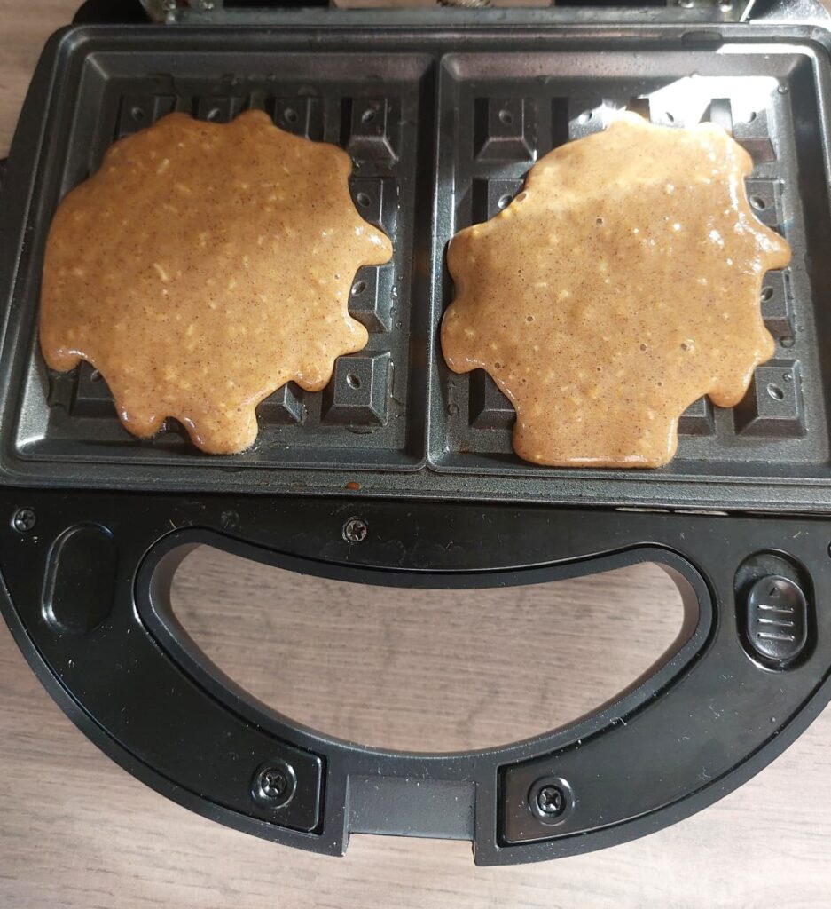 Pečení vaflí - Těsto na vafle rozlité na dvou rozpálených plotýnkách vaflovače těsně před zavřením a pečením.